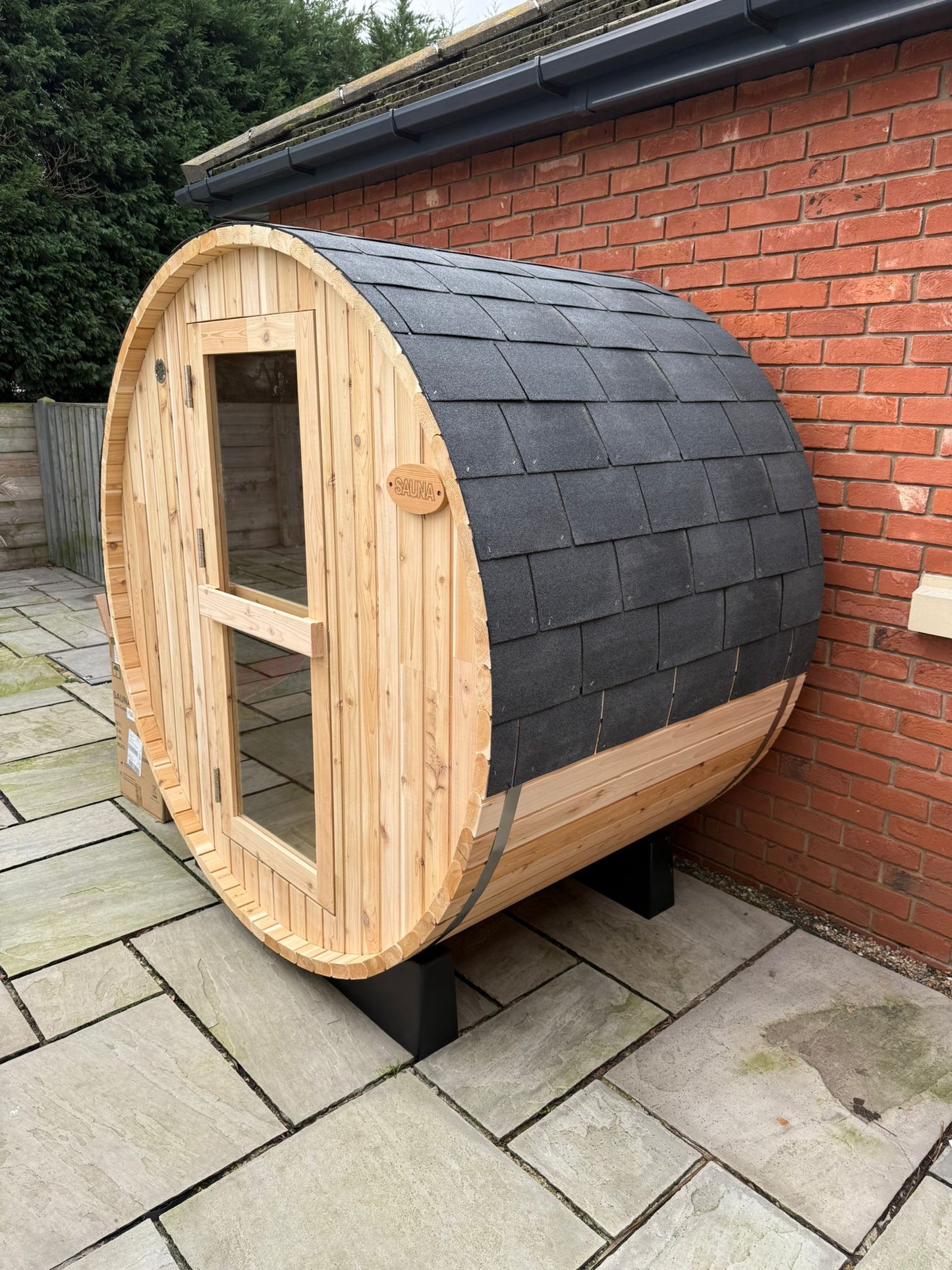 Two person barrel sauna on a garden patio beside a brick wall
