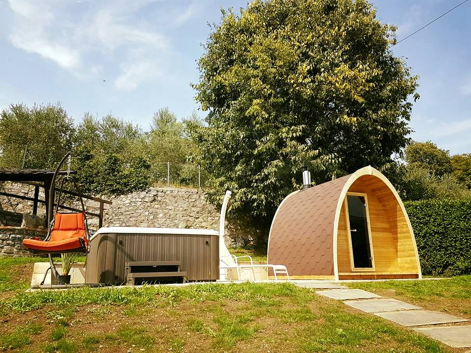 Kelo 300 sauna pod installed in a customer garden alongside a hot tub, with terracotta shingles and a wood-burner flue
