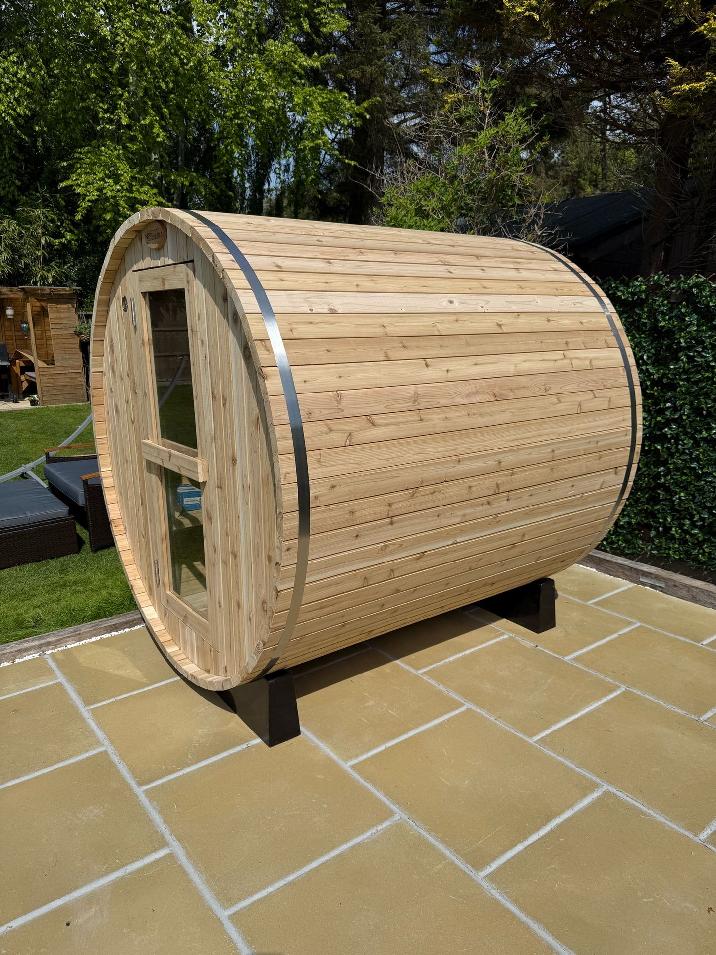 Four person barrel sauna in a garden with the door and window visible