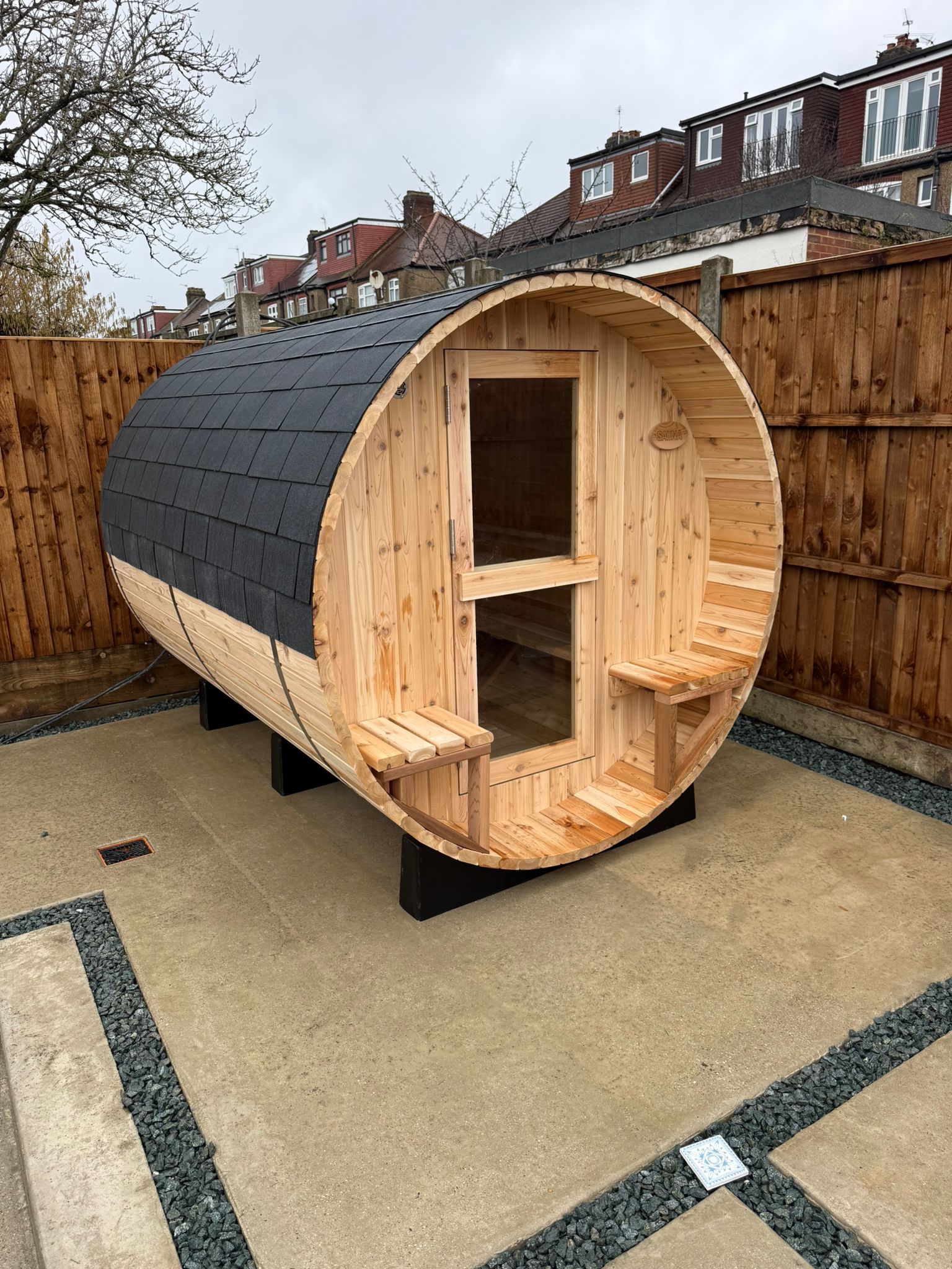 Six person barrel sauna with a porch, installed on a garden patio
