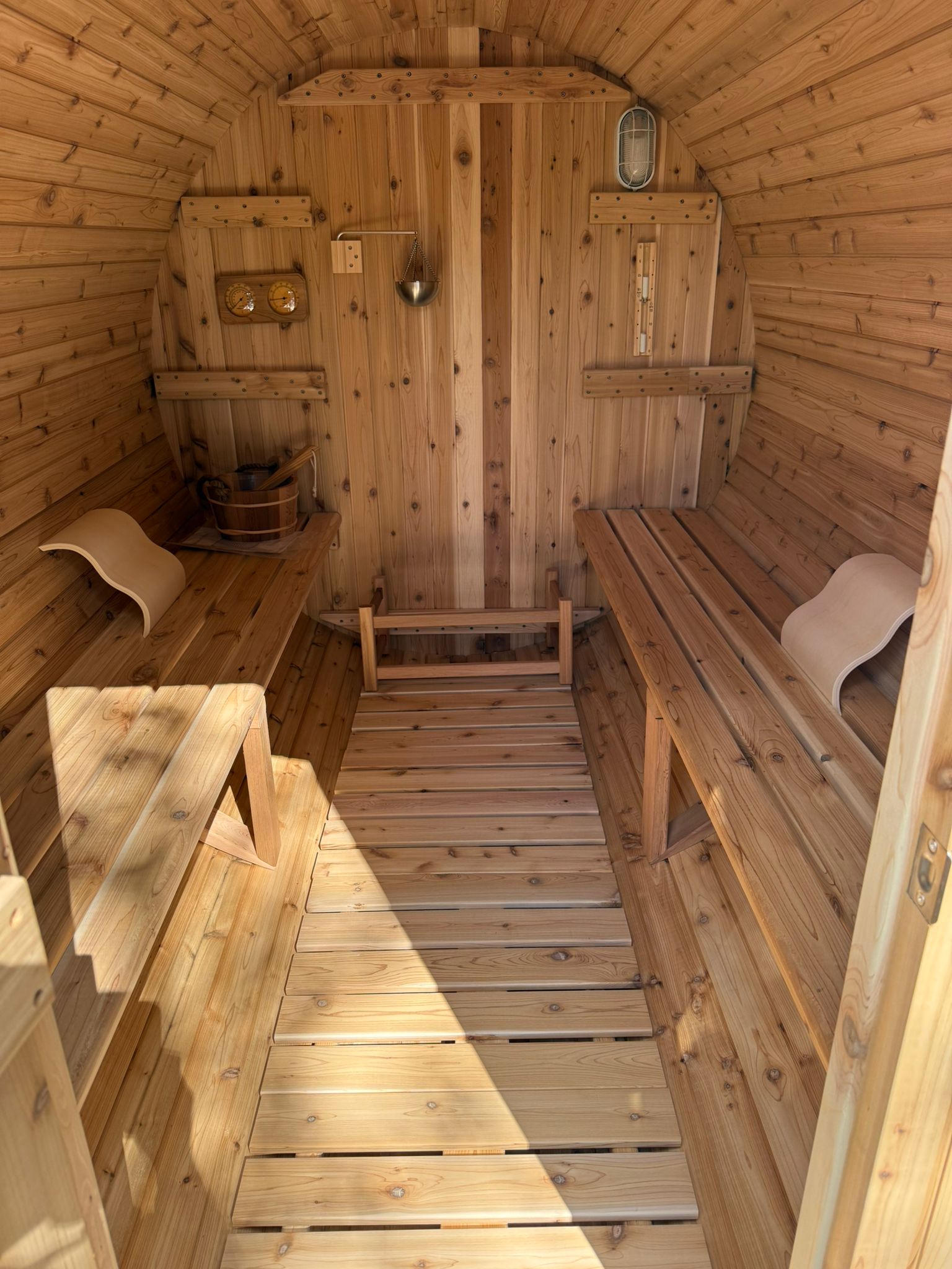 Six person barrel sauna installed in a garden, shown from the door end