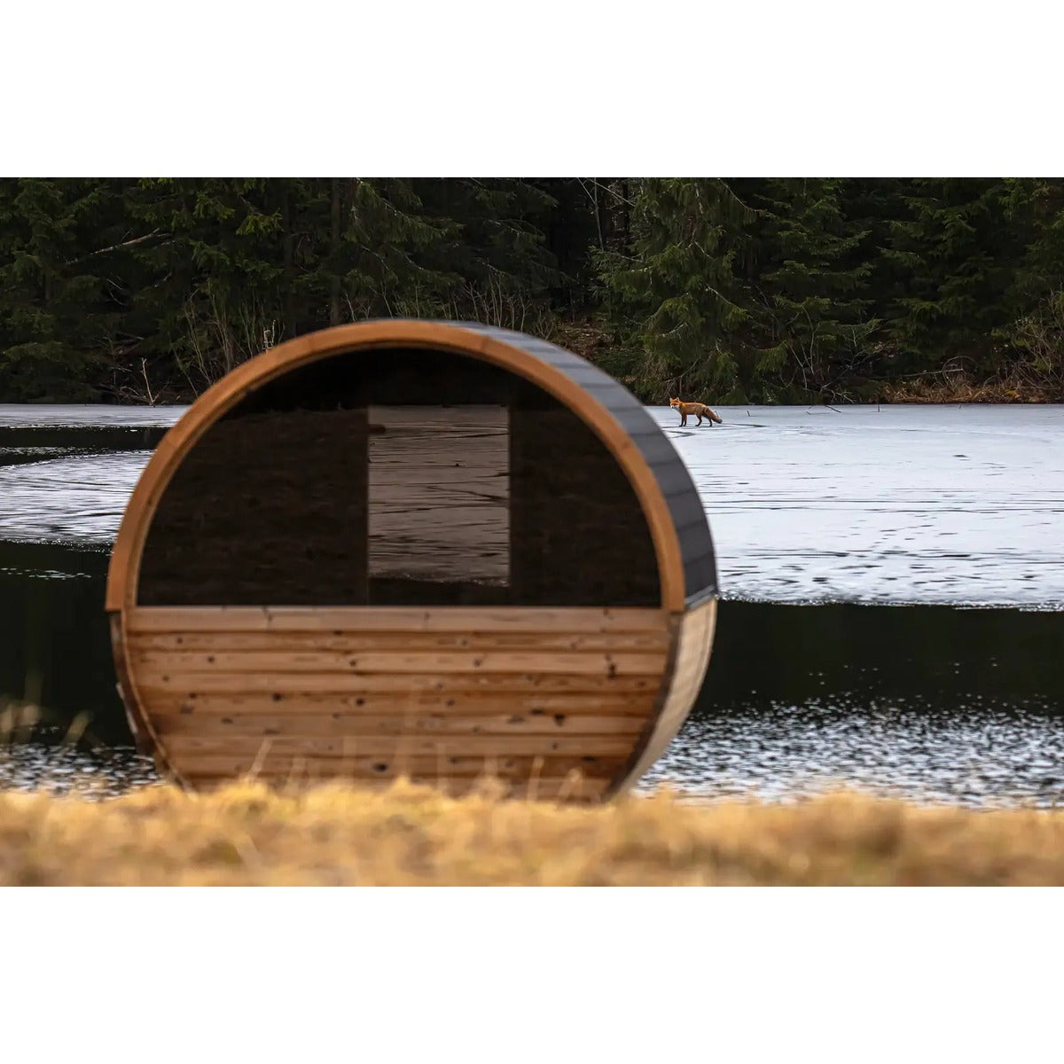 Front view of Hekla Barrel Sauna 210 by a lake (lifestyle image).