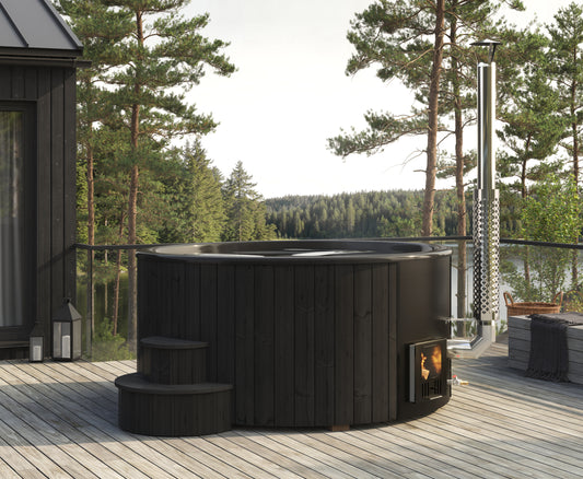 Steam & Oak Hehku 1650 XL wood-fired hot tub in black on a lakeside deck, stove lit