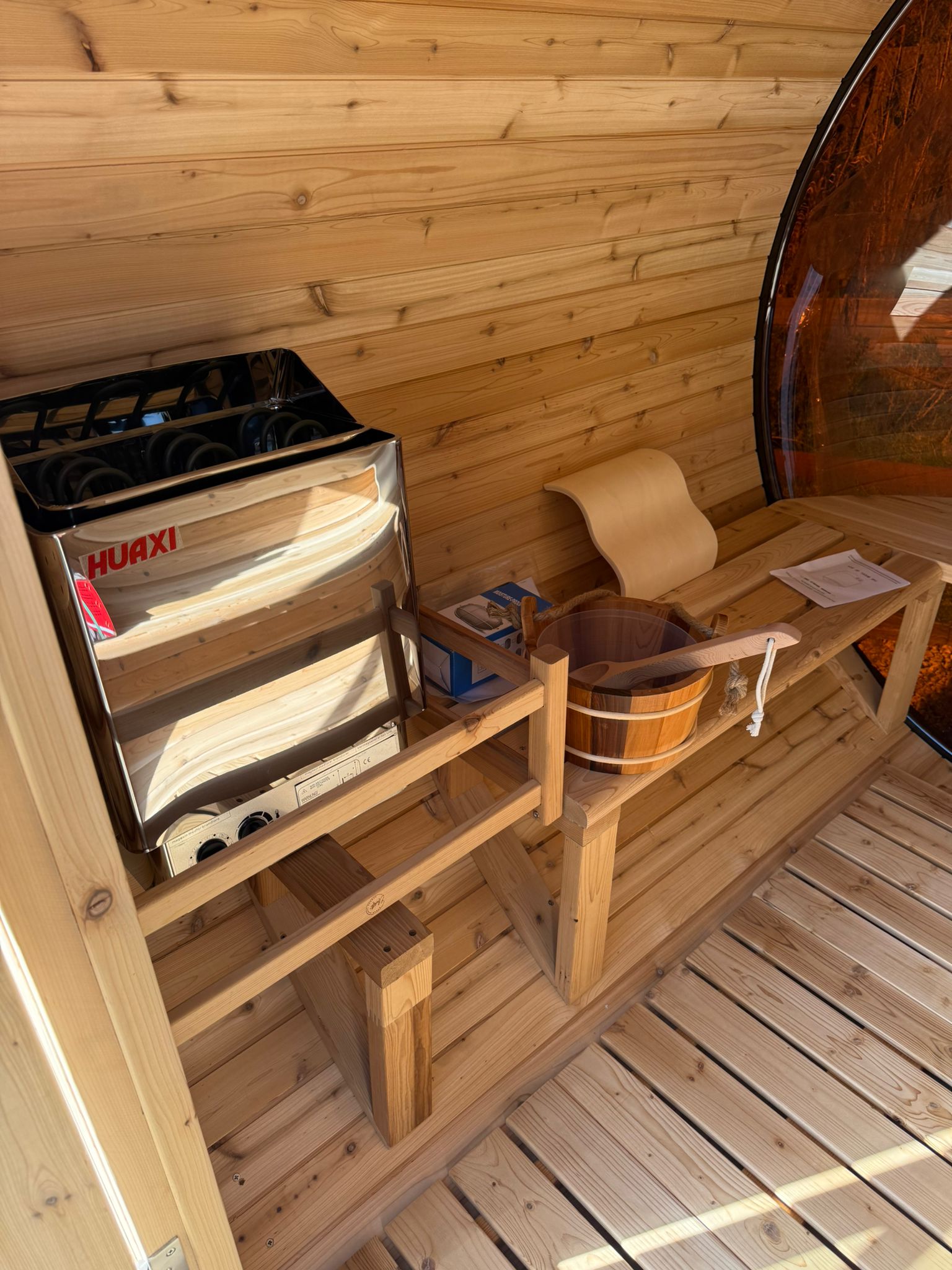 Panoramic barrel sauna installed on garden decking, with a shingled roof
